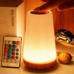 Lampe de chevet LED sans fil aux couleurs changeantes allumée et avec sa télécommande à côté, sur une table de chevet.