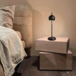 Lampe design sans fil noire allumée, posée sur des cubes de bois servant de table de chevet, dans une chambre à coucher.