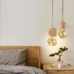 Lampe suspendue en bois naturel mise en scène dans une chambre à coucher, à la manière de lampes de chevet, à côté du lit.