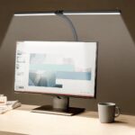 Lampe de chevet à pince à large spectre allumée et installée sur un bureau au-dessus d'un écran de PC.