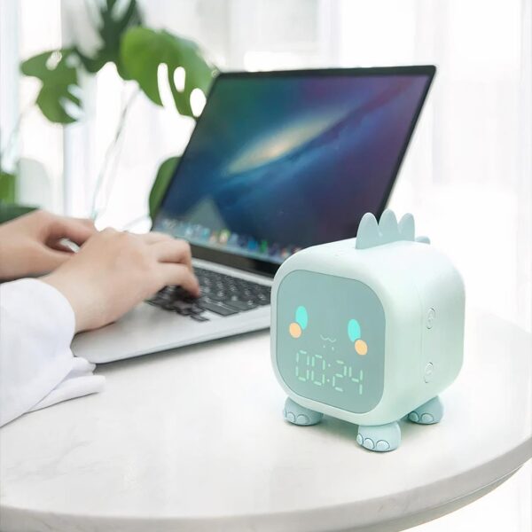 Lampe réveil dinosaure sur une table à côté de quelqu'un qui travaille sur ordinateur.