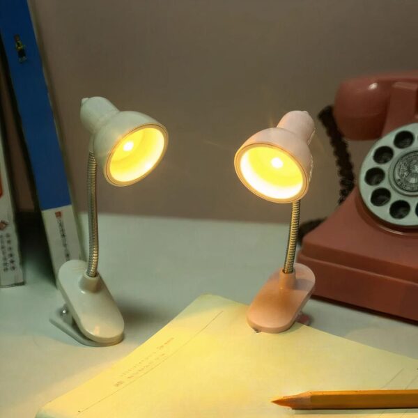 Mini-lampe à pince allumée qui éclaire un cahier sur un bureau.