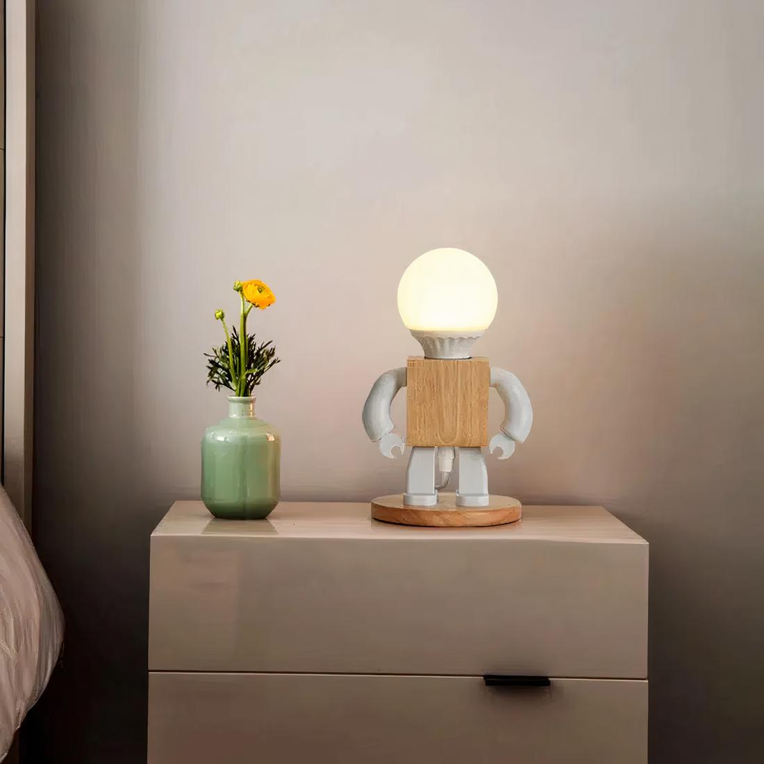 Img_12_2023_lampe_de_chevt_petit_robot_pour_garçon_1 Lampe de chevet petit robot pour garçon allumée et posée sur une table de chevet dans une chambre à coucher.
