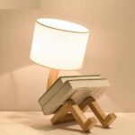 Lampe de lecture en bois articulée avec une pile de livres disposée sur les "jambes" de la lampe, sur un meuble.