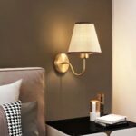 Lampe de chevet murale style scandinave allumée et fixée sur un mur à côté d'un lit dans une chambre à coucher.