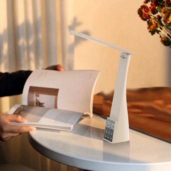 Lampe réveil LED rechargeable posée sur un bureau à côté d'une personne qui bouquine dans un salon.