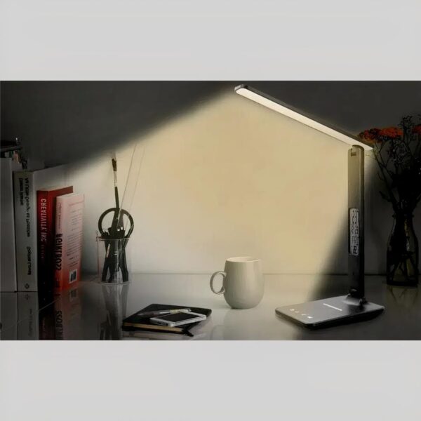 Lampe chargeur induction téléphone allumée sur un meuble avec des objets tels qu'une tasse de café et des livres.