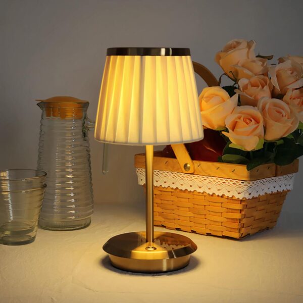 Lampe de chevet allumée avec un abat-jour plissé posé sur un support blanc avec des éléments de décoration à côté.