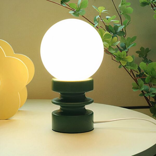 Lampe de chevet boule en bois massif allumée et posée sur une table ronde avec en arrière-plan une plante verte.