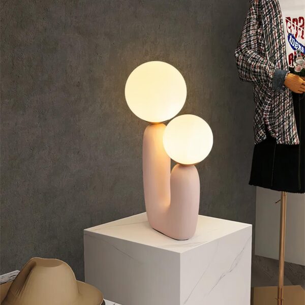 Lampe de chevet boule en verre, en version rose, allumée et posée sur une table design blanche, dans une chambre à coucher.