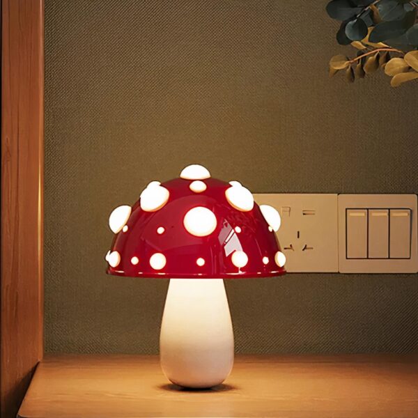 Lampe de chevet en métal et forme de champignon, en version rouge, allumée et posée sur un meuble en bois.