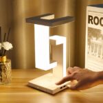 Lampe moderne au design carré allumée sur un support en bois avec des décorations autour, et le doigt d'une personne touchant le bouton d'allumage.