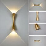 Lampe de chevet murale LED design en version dorée et allumée, fixée sur un mur gris.
