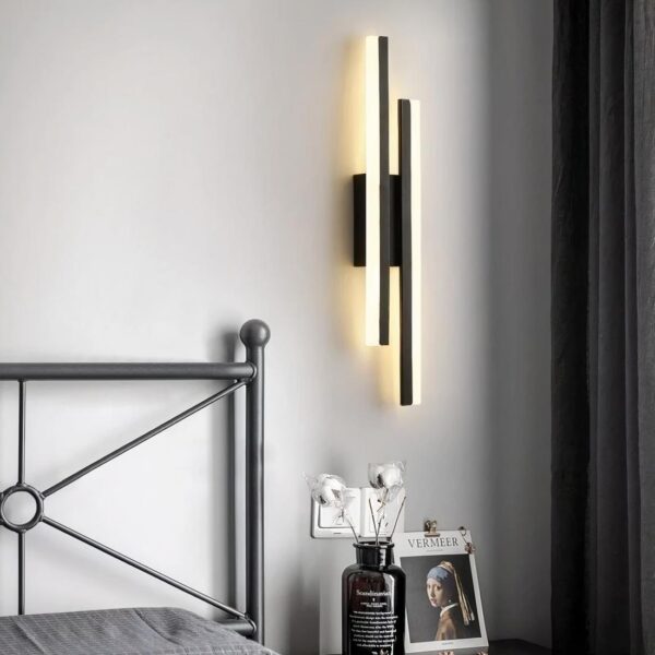 Lampe de chevet murale moderne à LED noire, installée auprès d'un lit dans une chambre à coucher et allumée.