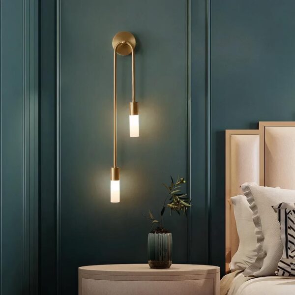 Lampe de chevet murale style scandinave dorée allumée et fixée au mur, à côté d'un lit, dans une chambre à coucher.