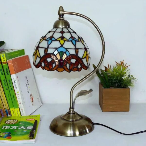 Lampe de chevet style Tiffany allumée, aux couleurs chaudes avec un pied courbé en métal doré, posée sur un support blanc