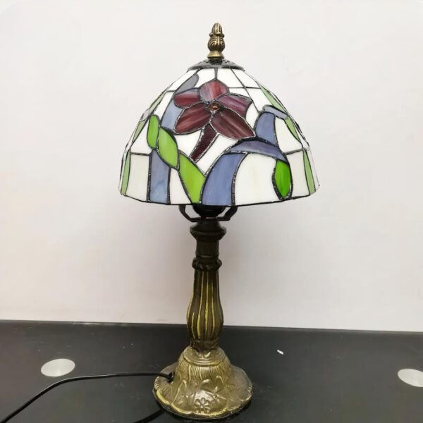 Lampe style Tiffany allumée, avec un abat-jour coloré avec une libellule, posée sur une table