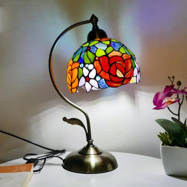 Lampe de chevet style Tiffany avec un abat-jour motif floral, allumée et posée sur une table blanche avec une orchidée à côté.