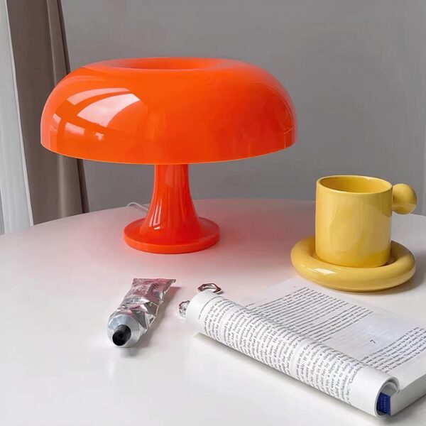 lampe de chevet orange posé sur une table près d'un livre et d'une tasse de café