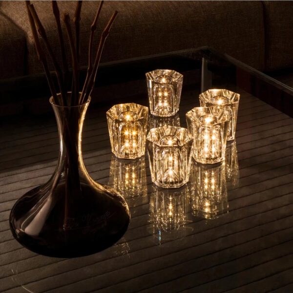 Lampe LED rechargeable en cristal allumée sur un meuble en bois et posée à côté d'un vase avec des fleurs, dans la pénombre pour accentuer leur luminosité.