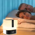 Réveil lampe de chevet multifonction allumé et mis en scène dans une chambre à coucher avec un couple dans son lit, prêt à dormir.