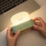 Lampe de chevet en forme de toaster dans les mains d'une personne près d'un ordinateur