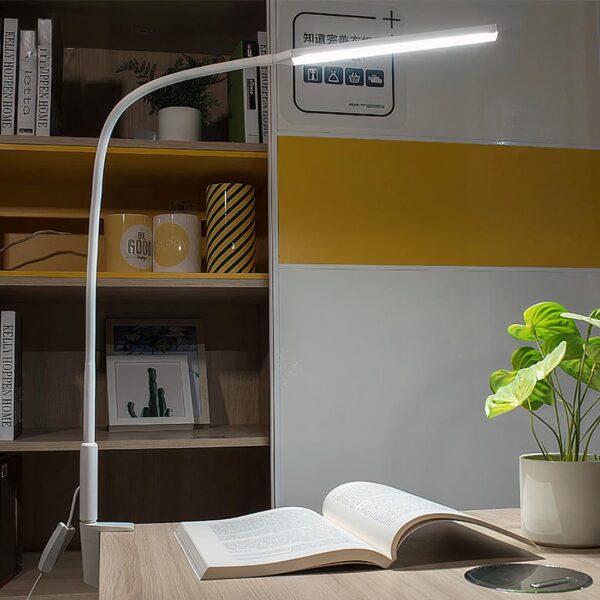 Lampe chevet à pince à bras long posé sur un bureau éclairant un livre