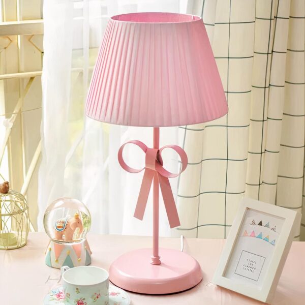 Lampe de chevet fille rose avec un nœud posé sur une table avec un cadre photo