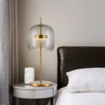 Une lampe de chevet vintage en verre fumé sur une table de chevet à côté d'un lit