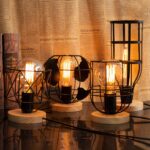 4 lampes de chevet filaires avec socle en bois de style industriel avec la douille fixée sur le rond en bois et les ampoules allumées. Chaque ampoule est entourée d'une grille en métal noire de forme géométrique différente. Du vieux journal en fond.