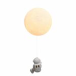 Astronaute se hissant sur cette lampe de chevet ronde en forme de lune allumée. Sur fond blanc.