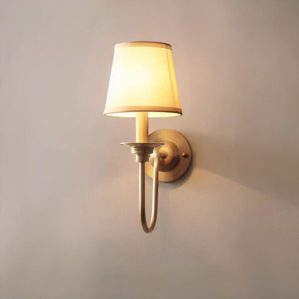 Lampe de chevet murale vintage avec col de cygne en cuivre et abat-jour en tissu beige. Fixée sur un mur gris. Lampe allumée.
