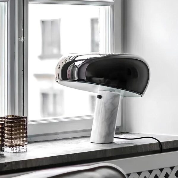 Lampe de chevet en forme de champignon, le pied est noir et blanc avec effet marbre, un interrupteur dessus. Le chapeau est noir brillant de forme ovale. La lampe est filaire sur le rebord d'une fenêtre.