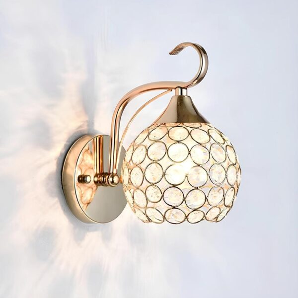 Lampe de chevet murale de couleur dorée. Socle rond au mur avec tige ondulée sur laquelle est suspendue une sphère ajourée avec des ronds de métal tout le tour laissant voir la lumière à l'intérieur. Jeu de lumière sur le mur.