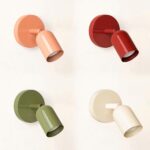 Quatre lampes de chevet murales dans chaque coin, en haut à gauche rose, en haut à droite rouge, en bas à gauche verte, en bas à droite blanche. Socle rond sur le mur et tête orientable comme un spot. Sur fond blanc.
