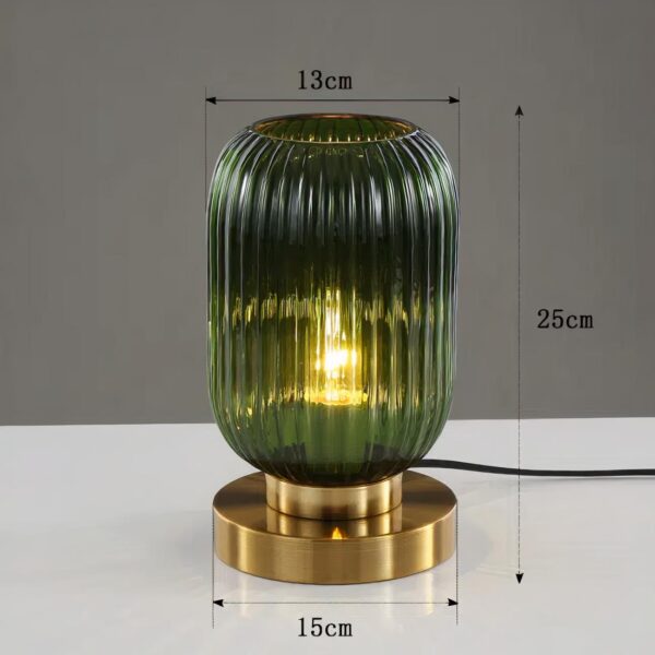 Lampe de chevet style vintage de forme cylindrique arrondi en verre strié vert avec ampoule allumée à l'intérieur. Le verre est posé sur un socle doré de forme ronde. La lampe est posée sur un support blanc, le fond est gris. Les dimensions sont affichées autour de la lampe.