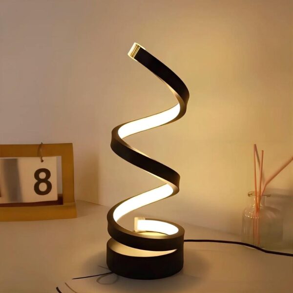 Lampe de chevet en forme de spirale de couleur noire posé sur un socle noir rond. Le long de la spirale, les LED diffusent une lumière chaude. A gauche, un calendrier avec le chiffre 8 sur un carré blanc. A droite, un récipient en verre avec 3 tiges roses.
