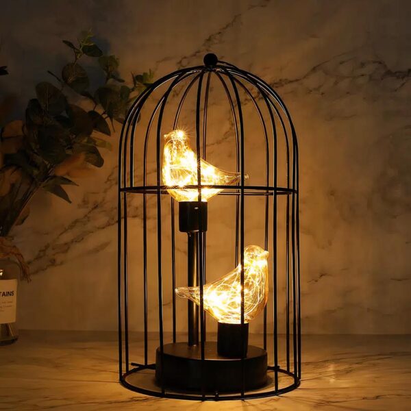 Une lampe sans fil en forme de cage en métal noire avec deux oiseaux en verre à l'intérieur