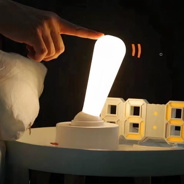Lampe de chevet sans fil style manette posé sur une table de chevet à côté d'un réveil
