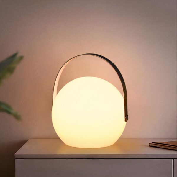 Une lampe de chevet sans fil en boule avec une anse posé sur une table et allumée