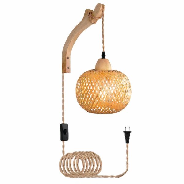 Lampe de chevet suspendue avec fixation murale en bois. Son câble est muni d'un interrupteur et passe sur la fixation en bois avec en suspension un abat-jour ovale en rotin. Sur fond blanc.
