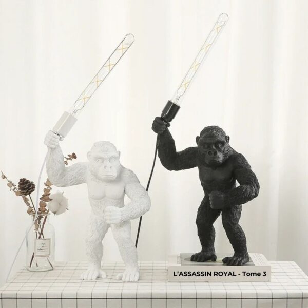 Lampe de chevet jungle gorille debout dans les deux versions, blanc et noir, posées sur un petit meuble en bois blanc, avec à côté un petit vase avec des fleurs séchées.